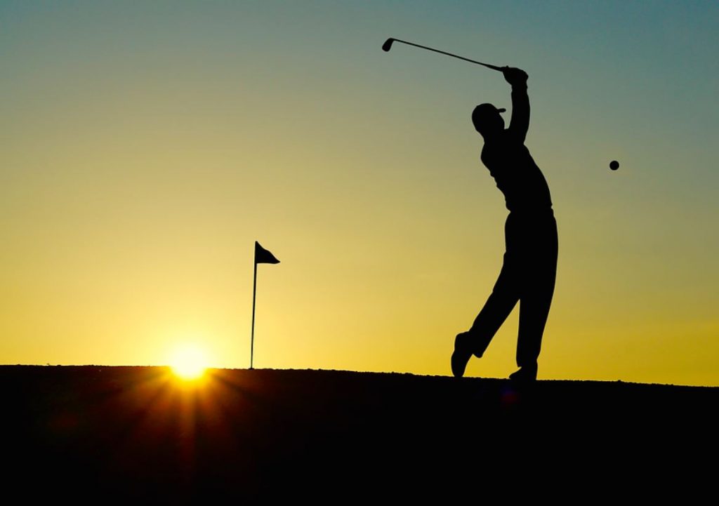 Silhouette of the back of a man swinging a golf club with the sun setting in the background. | Golf clubs around Jacksonville, AR.