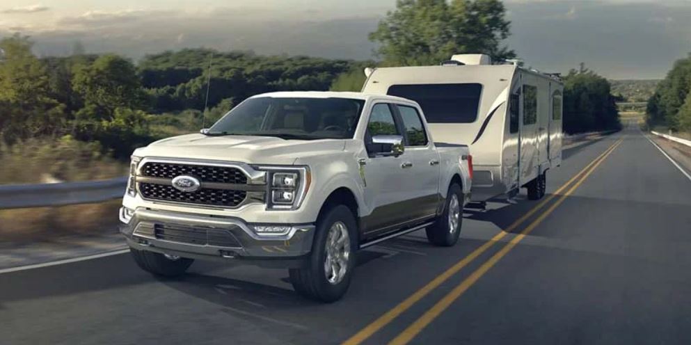 A white 2022 Ford F-150 pulling a camper on the highway. | Ford dealer in Jacksonville, AR.
